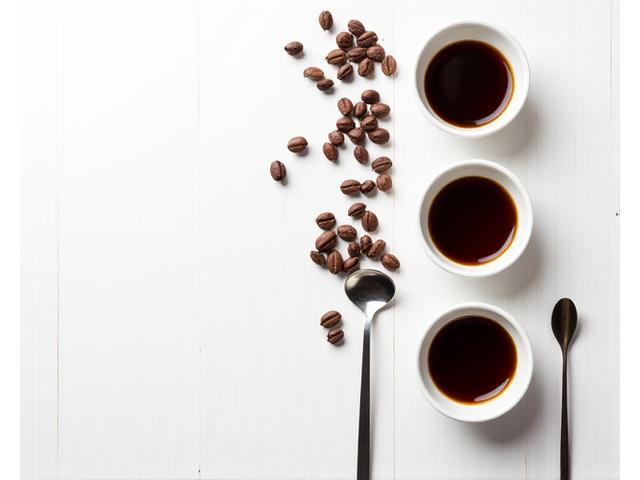 Beberapa cawan kopi yang berlainan di atas meja dengan biji kopi panggang dan peralatan cupping, sedia untuk penilaian aroma dan rasa.